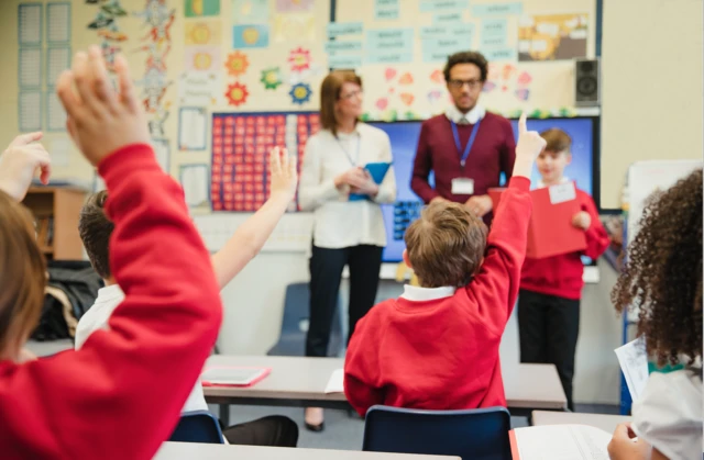 Stock image of children with their hands up in school