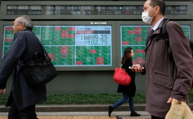 Pedestrians walk past a quotation board displaying share price numbers of the Tokyo Stock Exchange in Tokyo (March 17, 2020).