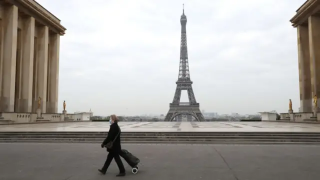 A tourist in a protective mask walks past the Eiffel Tower on 18 March