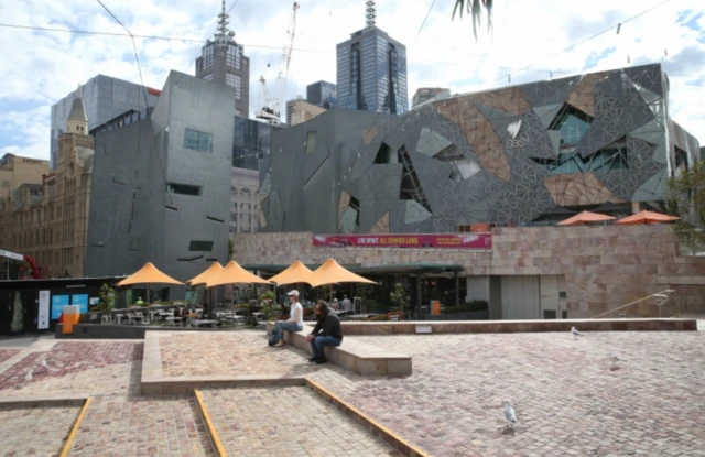 Two people sit a distance from each other in Melbourne's nearly-empty Federation Square