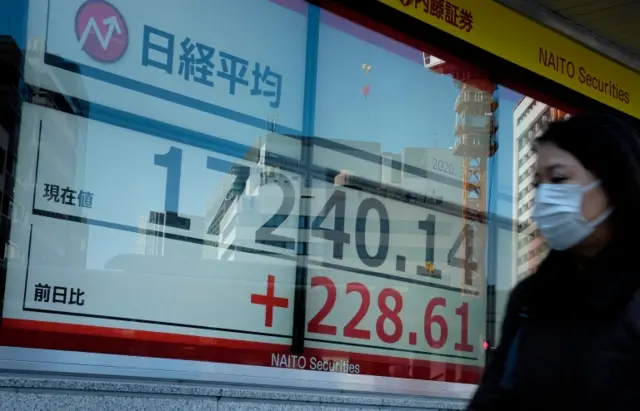 A pedestrian walks in front of a quotation board displaying the share price numbers of the Tokyo Stock Exchange in Tokyo (March 18, 2020).