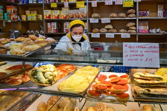 A shopkeeper wearing a face mask picks up a pizza at a food shop in Rome