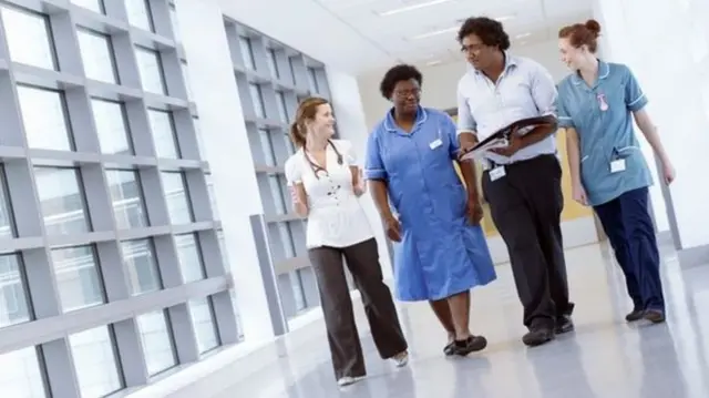 NHS staff in uniform walk in a corridor