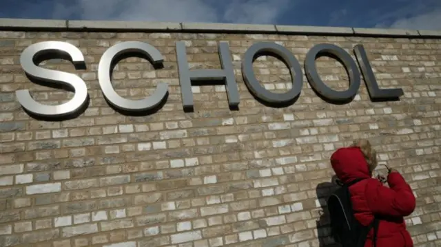 Child stood under a sign that reads: School