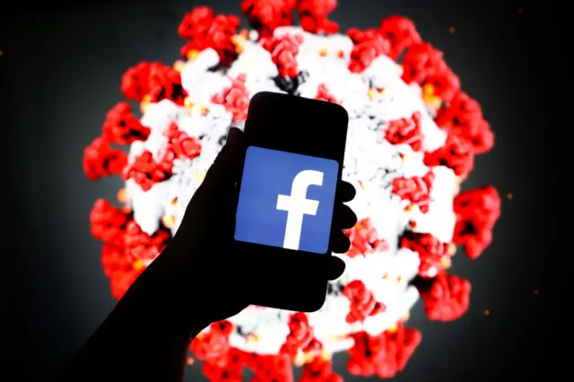 Facebook logo displayed on a mobile phone screen photographed on SARS-CoV-2 illustration graphic background.