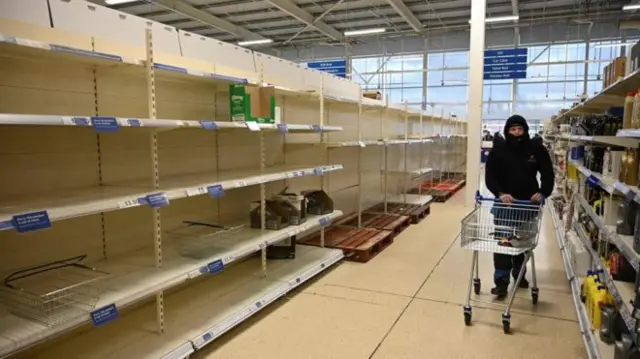 A woman wheels a shopping trolley down a stripped aisle in a supermarket