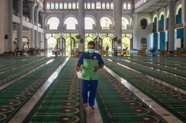 A worker wearing a face mask sprays disinfectant inside the Al Akbar mosque before Friday prayer in Surabaya, East Java province on March 6, 2020.