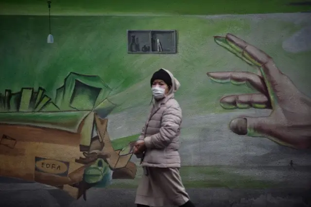 A masked woman walks by an image on a wall in Wuhan in central China's Hubei province