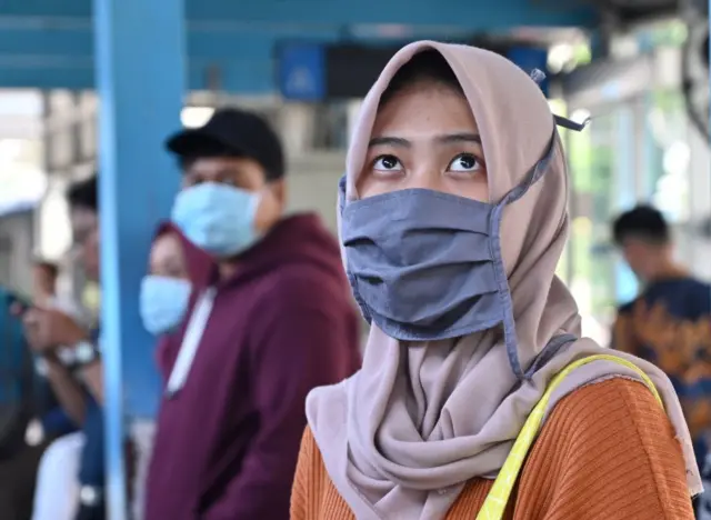 A woman wearing a face mask stands on a street in Jakarta