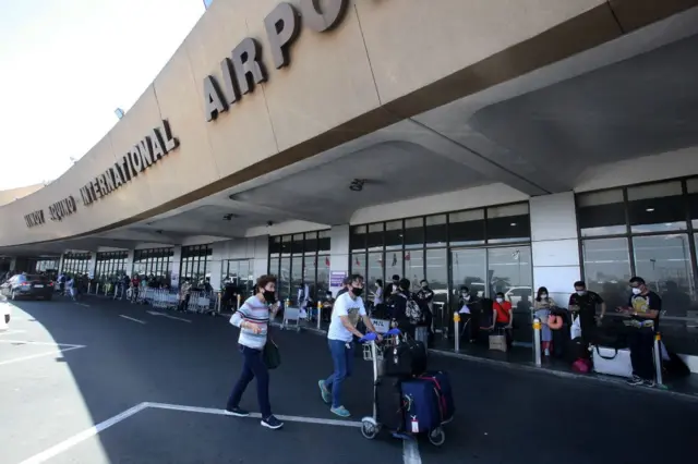 Passengers queue up outside as they wait for their flights out of the country at Manila's international airport