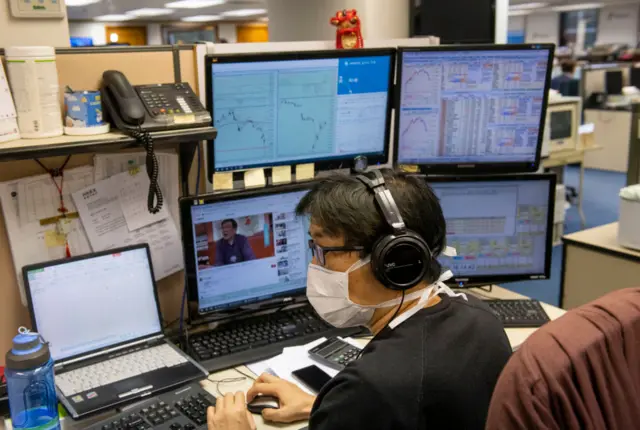 A stock broker surrounded by computer screens follows the Hang Seng Index results in Hong Kong.