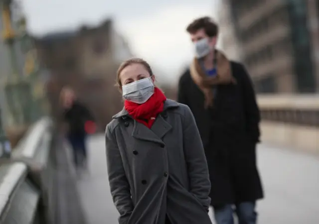 People wearing protective face masks walk across Westminster bridge in London