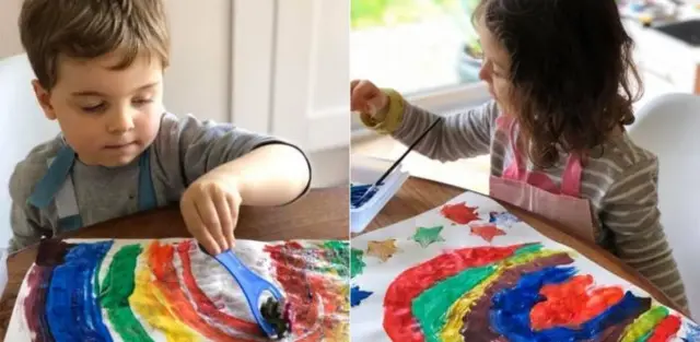 Two children paint rainbows on paper