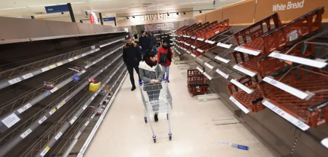 Shoppers look over empty shelves at a Tesco supermarket in London
