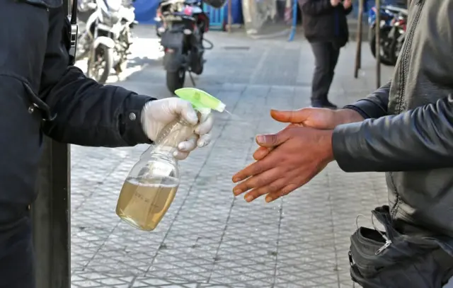 An Iranian man wearing a face mask sprays alcohol on the hands of another man. Photo: March 2020