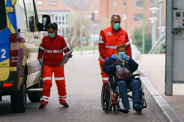 A health worker pushes a woman on a wheelchair outside a hospital in Spain