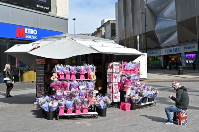 A flower seller sits on a stool waiting for business ahead of Mother's Day in Birmingham, central England. Photo: 21 March 2020