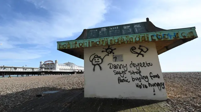 Graffiti is seen on the beach telling people to stop panic buying food in Brighton, on the south coast of England on March 21, 2020, a day after the British government said it would help cover the wages of people hit by the coronavirus outbreak as it tightened restrictions to curb the spread of the disease.