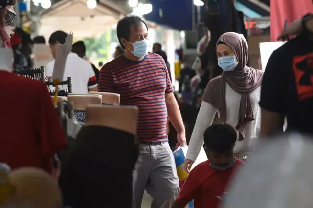 People wearing wearing masks walk past shops in Singapore. Photo: 21 March 2020