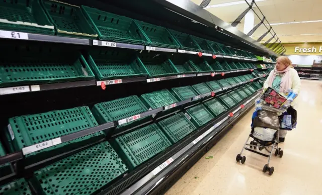 An elderly woman looks over empty shelves at a Tesco supermarket in London,