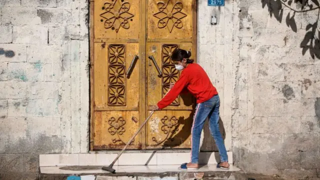 Girl in Gaza with protective mask on sweeping a doorstep