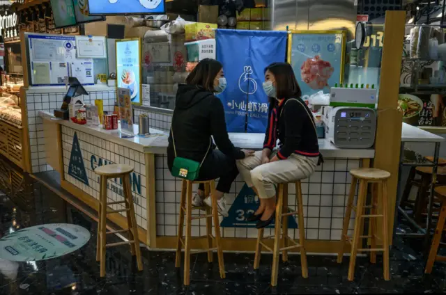 Chinese women wear protective masks as they talk at a restaurant on March 22, 2020