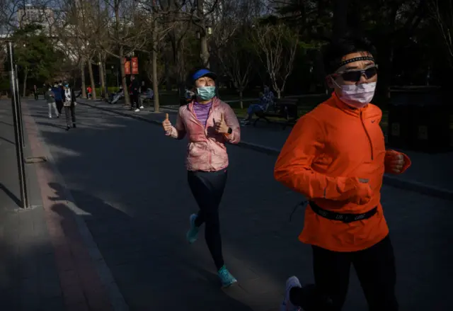 A Chinese man and woman wear protective masks as they run at Ritan Park