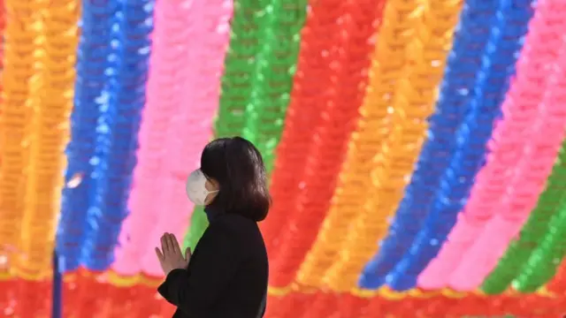 A Buddhist follower wearing a face mask prays under rows of lotus lanterns ahead of Buddha's birthday at Jogyesa Temple in Seoul on March 23, 2020