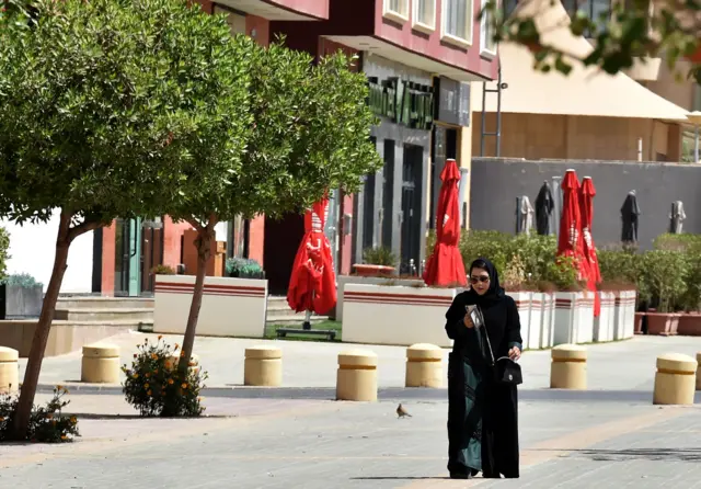 A picture taken on March 16, 2020 shows a woman walking past a closed restaurant in the Saudi capital Riyadh.