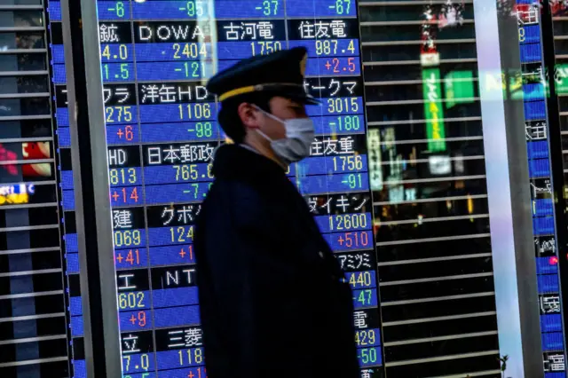 A passerby with a face mask walks past a stock board in Tokyo's Nihonbashi district showing the Nikkei average index falling on the Tokyo Stock Exchange.