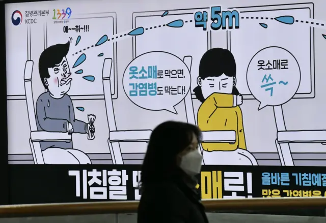 A woman wearing a face mask walks past a poster showing preventative measures against infectious diseases, at a railway station in Seoul on March 21, 2020.