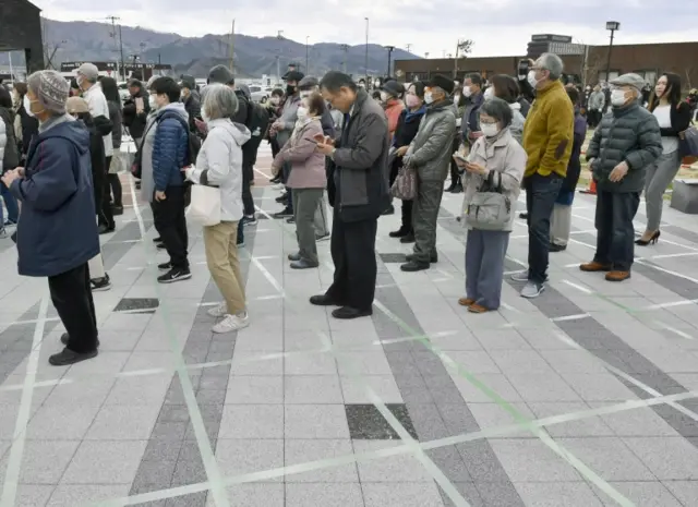 People wearing protective face masks form a line while keeping distance from others as they try to watch the Olympic flame during the Tokyo 2020 Olympics Flame of Recovery tour in Ofunato