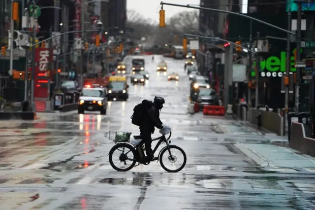 A delivery person rides their bike across 7th Avenue in a mostly deserted Times Square