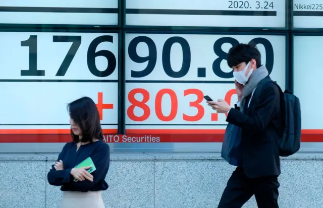 Pedestrians walk past a quotation board displaying the share price numbers for early trading on the Tokyo Stock Exchange in Tokyo (March 24, 2020).