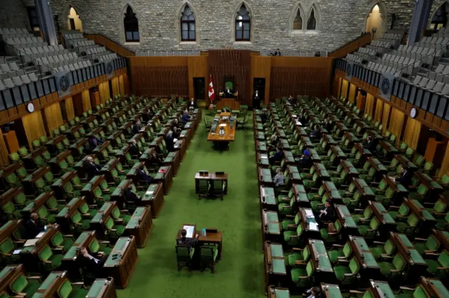 Canadian MPs in a nearly empty in the House of Commons as legislators convene to give the government power to inject billions of dollars in emergency cash