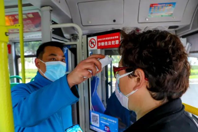 A citizen wearing face mask has her body temperature measured as she gets on a bus in Wuhan