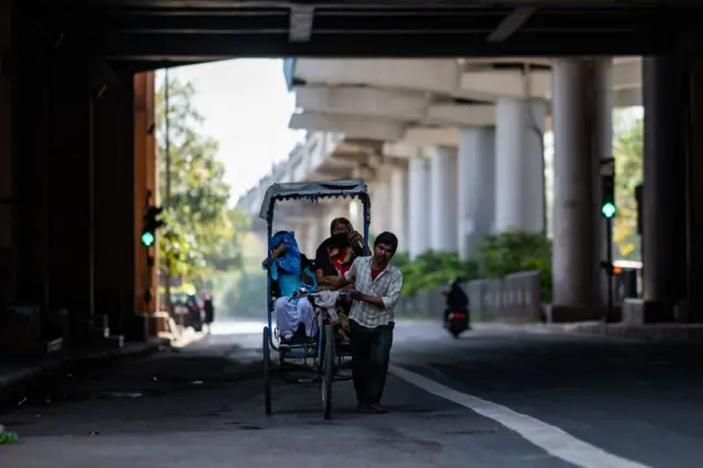 A rickshaw driver transports his passengers along a deserted street during the first day of a 21-day government-imposed nationwide lockdown