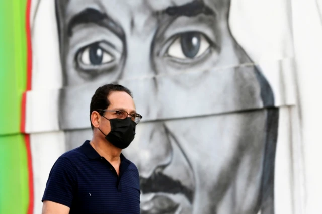 A man wearing a face mask walks past a mural of King Salman in Riyadh, Saudi Arabia (25 March 2020)