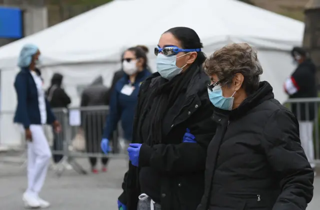 People wearing masks and goggles pass by a COVID-19 screening tent outside the Brooklyn Hospital Center