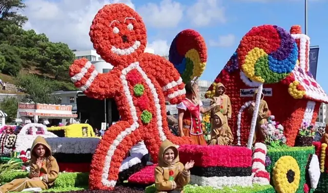 Battle of Flowers float with a gingerbread man made of flowers and children sitting alongside