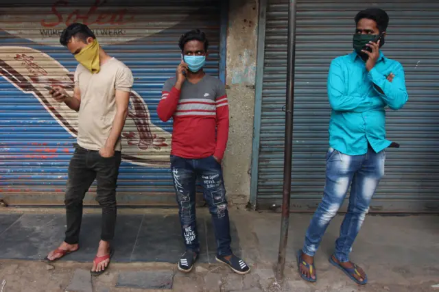 Men wearing protective face masks use mobile phones during a curfew in response to the outbreak of the Coronavirus (COVID-19) pandemic on March 24, 2020 in Mumbai, India.