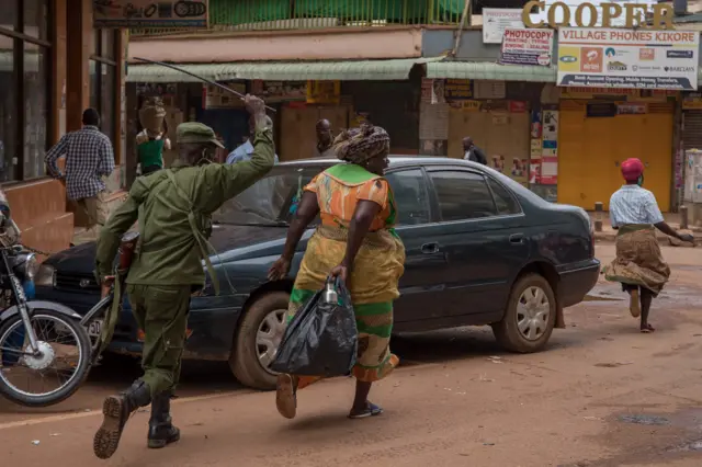 A police officer chases away a woman on a street in Kampala, Uganda - 26 March