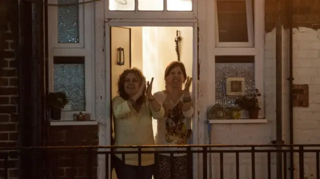 Two women clap in a doorway