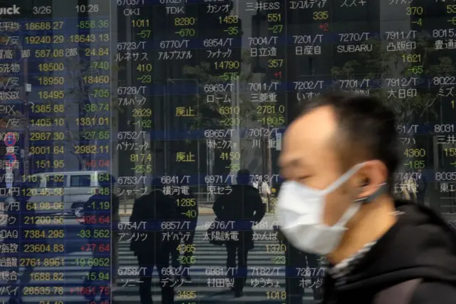 Pedestrians walk in front of a quotation board displaying stock prices on the Tokyo Stock Exchange.