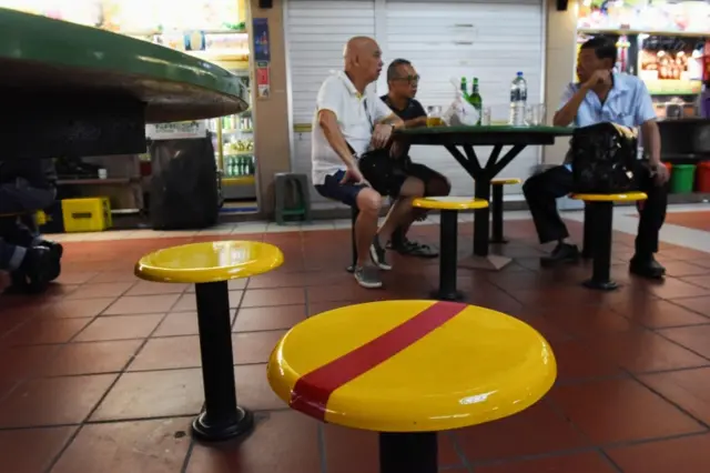 Customers take their meal while some chairs are marked with red tapes as authorities implement social distancing at a hawker centre, amid fears about the spread of the COVID-19 novel coronavirus in Singapore on March 18, 2020.