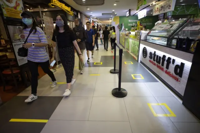 People wearing face masks walk past social distancing signs on the floor at an eatery in a shopping mall in Singapore, 26 March 2020.