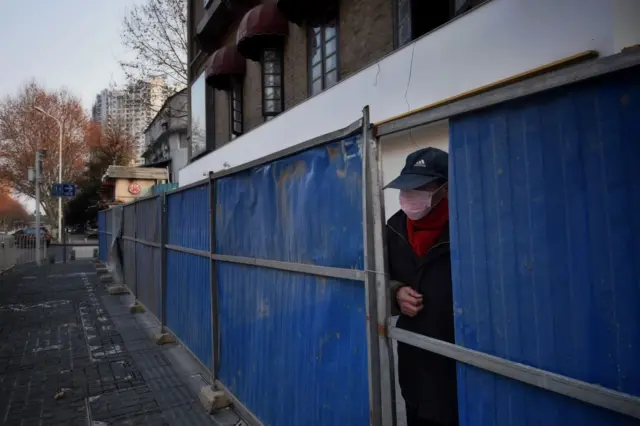 A masked man looks out from the fence set up to curb the COVID epidemic in Wuhan