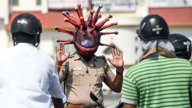 Chennai police officer wearing a coronavirus helmet, facing people on the street and holding his hands up