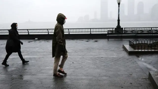 Pedestrians in Brooklyn walking against the Manhattan skyline in New York, wearing coronavirus masks