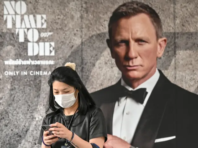 A woman wearing a face mask amid fears of the spread of the Covid-19 walks past a poster for the new James Bond film "No Time to Die" in Bangkok, 28 February 2020